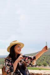 Single Latin adult woman with hat uses her travel cell phone to stay connected, take photos, selfies, video calls, locate herself on the map to share experiences
