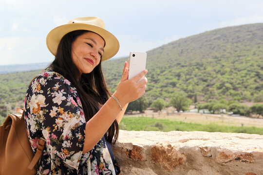 Single Latin adult woman with hat uses her travel cell phone to stay connected, take photos, selfies, video calls, locate herself on the map to share experiences

