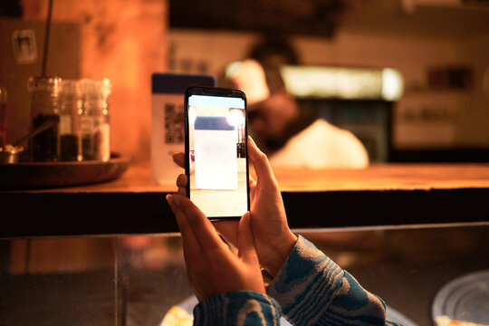 Person with phone camera scanning QR bar code for online menu at a modern restaurant, shop or cafe at night. Hand of a woman taking photo scan for website information using modern technology