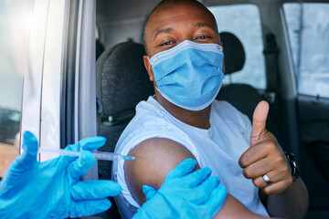 Drive thru covid and corona virus vaccine site as a public service for the people. Man giving thumbs up and endorsing the jab while wearing a mask to avoid infection, approving being vaccinated - obrazy, fototapety, plakaty