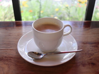 白い陶器のカップに入ったカフェオレおよび窓越しの花