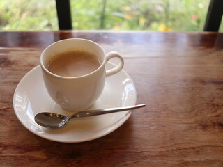 白い陶器のカップに入ったカフェオレおよび窓越しの花