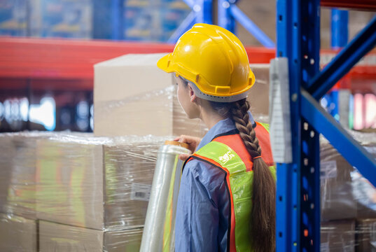 Female worker wrapping boxes in stretch film at warehouse, Worker wrapping stretch film parcel on pallet in factory warehouse