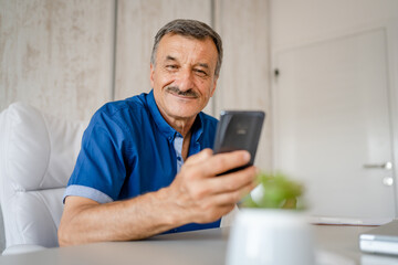 senior man hold cup of coffee and mobile phone while sitting at work