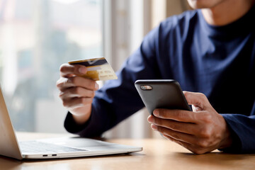 Man holding credit card and using smartphone at home online shopping ecommerce internet banking spend money work from home concept.