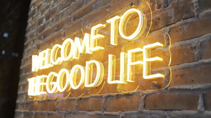 Cartel de neón naranja que dice "bienvenido a la buena vida" en el fondo de la pared de ladrillo, vista cercana