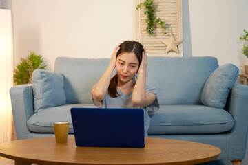 夜にリビングでパソコンを見て頭を抱える女性