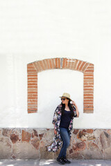 Single latin adult woman with sunglasses and hat walks through the colonial style streets with cobbled white wall, relaxed she strolls as a tourist on vacation or weekend
