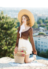 Pretty girl in a straw hat poses kneeling against the background of the city