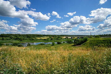 Summer sunny day over the river. Calm, relaxing rural landscape with white clouds on blue sky.