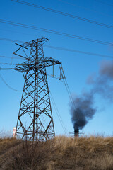 High-voltage electricity transmission line with a large pole against the background of a smoking pipe