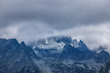 Fototapeta na wymiar Tatras high mountain pass in dramatic atmosphere. Overcast cloudscape with snowy mountain peak. Abstract high mountain cloudy sky background, travel adventure. Extreme hiking, recreational scenic