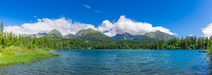 Scenic panorama over lake in park High Tatras. Strbske Pleso, Slovakia. Wonderful summer landscape. Picturesque view of nature. Amazing natural wide background, green forest, blue sunny sky clouds