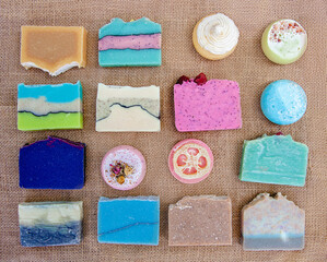 Flat layout of multi-colored round and square pieces of homemade soap on burlap. Set of bright soap