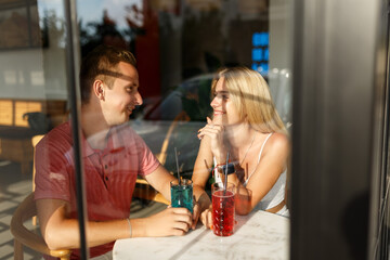 Romantic loving couple drinking lemonade, having a date in the cafe, view through window.