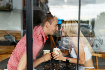 Romantic loving couple drinking coffee, having a date in the cafe, view through window.