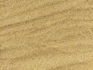 The background is made of fine sand. Sandy background. Sand lies in waves on the beach. Small granules of sand with inclusions of black pebbles