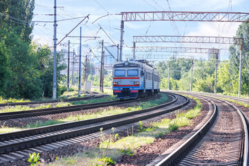The outgoing old train rides along the railroad against the backdrop of city buildings in a sunny haze.