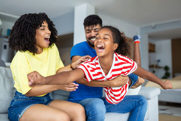 Happy African American dad and mom with excited proud daughter kid, playing flying superhero,...
