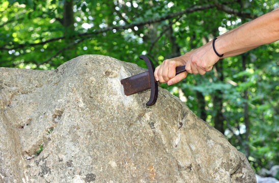 Mighty arms of the knight trying to draw the sword into the stone in the forest