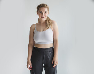 Young woman with overweight poses against a gray background in a crop top and yoga pants. Daily comfortable clothes for home and leisure on a curvy girl show her body. Self acceptance  body positivity