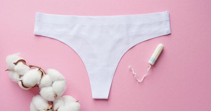 Composition of women's underpants, a branch of cotton, a tampon and a sanitary pad on a pink background. Period. Looped 4K stop motion animation