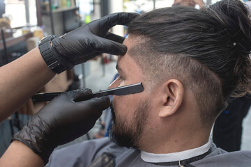 A barber uses a straight edge razor to shave and shape the edge of a clients scalp from hairline...