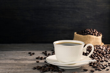 Black coffee in a white coffee cup with hot steam and coffee beans placed on a wooden table on a dark background. in a warm atmosphere
