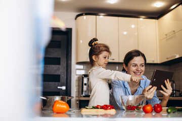 Mothee with daughter cooking usinf tablet at the kitchen