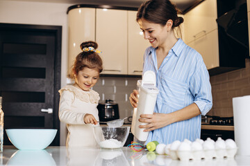 Mother with daughter cooking and pouring milk into the bowl with flour