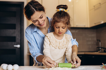 Fototapeta premium Mother with daughter preparing dough using rolling pan at the kitchen