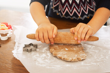 A close up dough.Child hands using rolling spin for gingerbread cookies. Christmas family traditions. Leisure of the child during the New Year holidays.