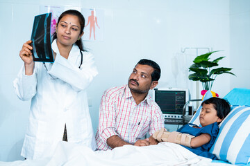 Doctor explaining kids x ray report about broken hand to father at hospital before surgery - concept of pediatrician, childcare service and injury.