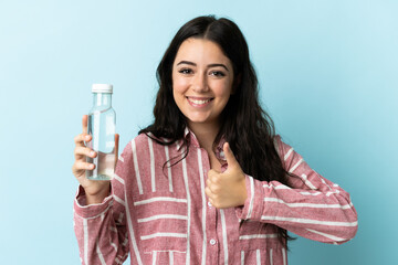 Young woman with a water isolated on blue background with thumbs up because something good has happened