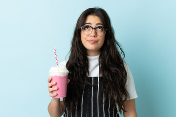 Young woman with strawberry milkshake isolated on blue background and looking up
