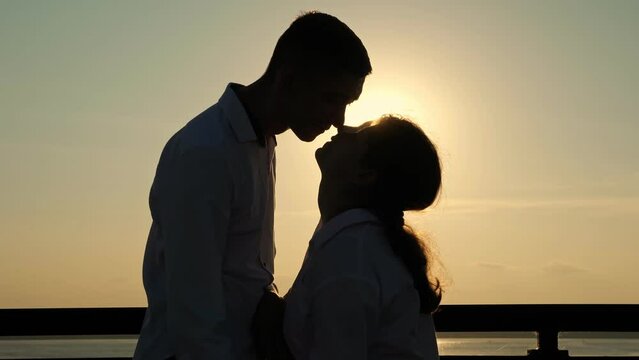Silhouettes of young loving people spending time together. Man and woman with cerebral palsy touch noses showing love and trust standing against back sunset