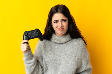 Woman playing with a video game controllerisolrted on yellow background with sad expression