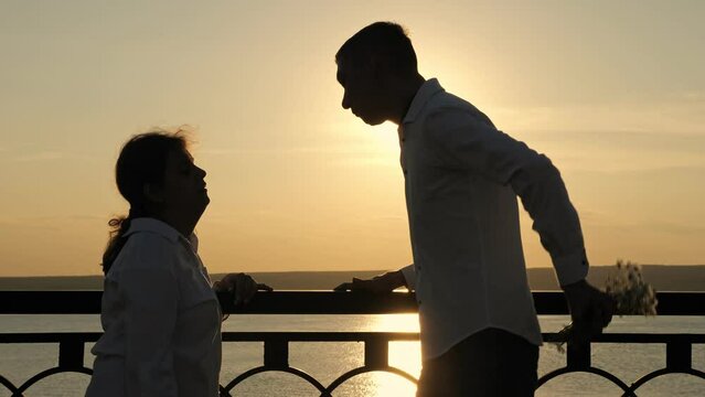 Young man with cerebral palsy gives present for woman against river. Male partner gives bouquet of flowers for woman at back sunset. Man shows love and appreciation