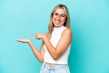 Young caucasian woman isolated on blue background holding copyspace imaginary on the palm to insert an ad