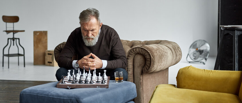 Senior man playing chess with himself in armchair