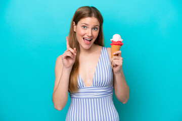 Young caucasian woman in swimsuit eating ice cream isolated on blue background pointing up a great...
