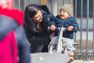 A Wonderful full of happiness dark-skinned five years of age boy on a see saw spending lovely time together with his attractive caucasian mother on a playground for kids. High quality photo