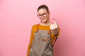 Woman with apron isolated on pink background doing coming gesture