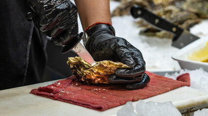 Unrecognizable woman opening the shell of a fresh oyster at a market in Arcachon (France), selective focus on the left hand glove. © Carlos