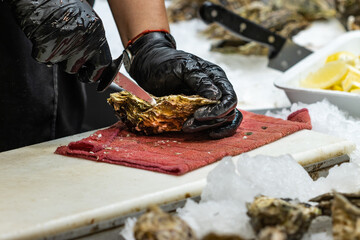 Unrecognizable woman opening the shell of a fresh oyster at a market in Arcachon (France),...