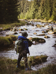 a boy on his way to camping in the woods. standing by a mountain river. equipped with his backpack and equipment. ready for adventure. 