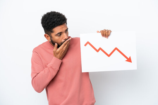 Young Brazilian man isolated on white background holding a sign with a decreasing statistics arrow symbol with surprised expression