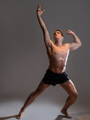 Obraz premium young muscular man in an expressive pose, artistic pose of the hero with outstretched arms. Beautiful muscles. extraordinary athletic body. Portrait on a gray background