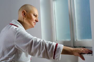 Senior depressed female cancer patient standing beside hospital window
