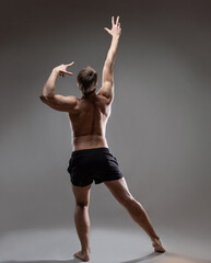 Fototapeta premium young muscular man in an expressive pose, throwing his hands up. Beautiful muscles. extraordinary athletic body. Portrait on a gray background